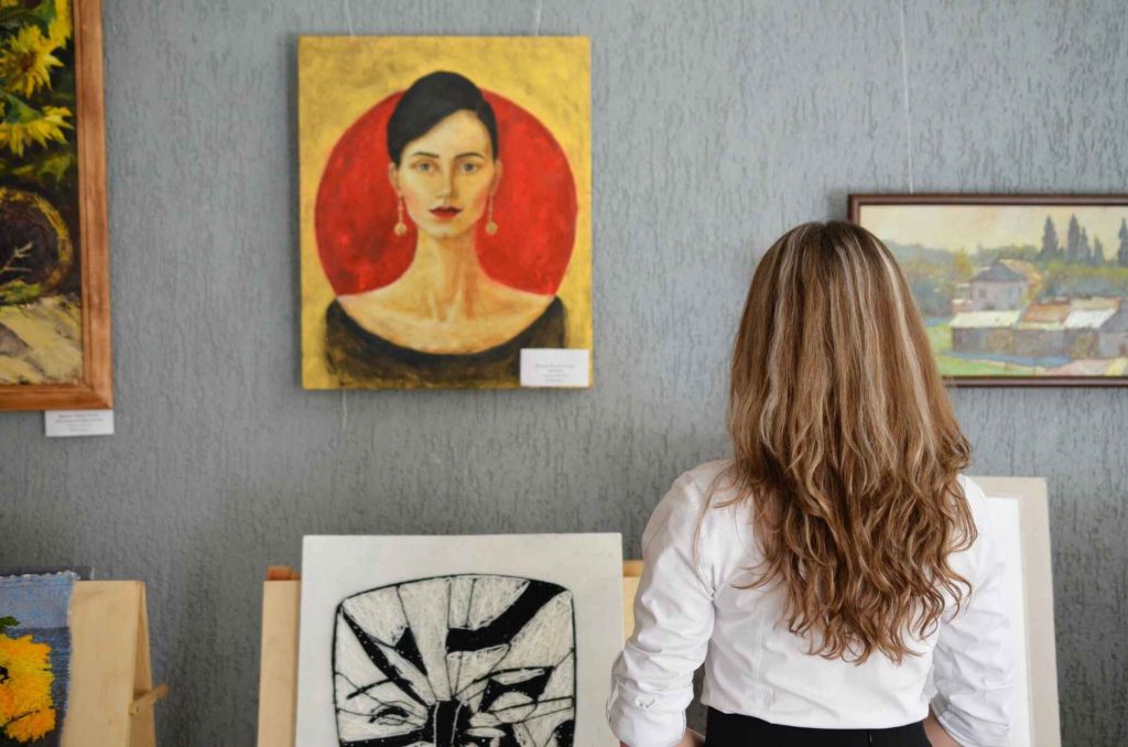 Woman looking at paintings displayed on a gray wall