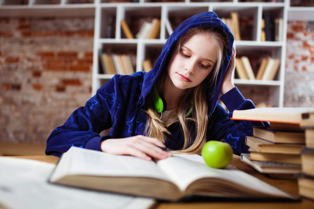 Woman wearing a blue hoodie while reading one of the stacked books on her table