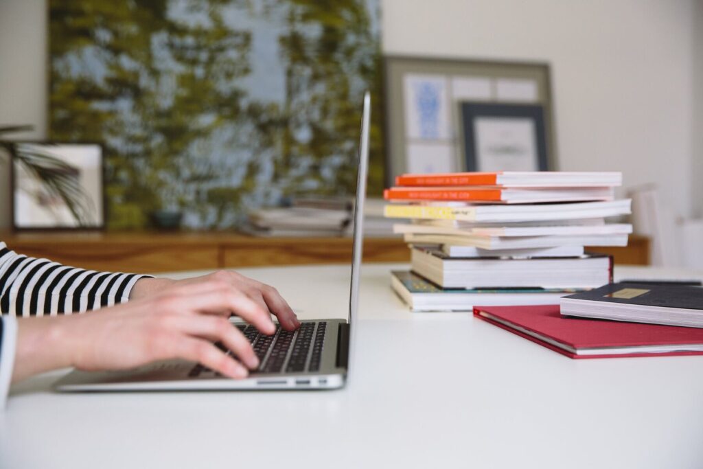 Person using their laptop while a stack of books are near her table