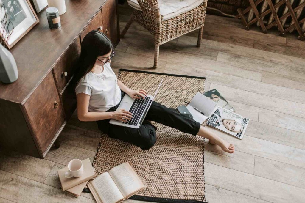 Woman sitting on the floor with books and magazine lying around, while using her laptop