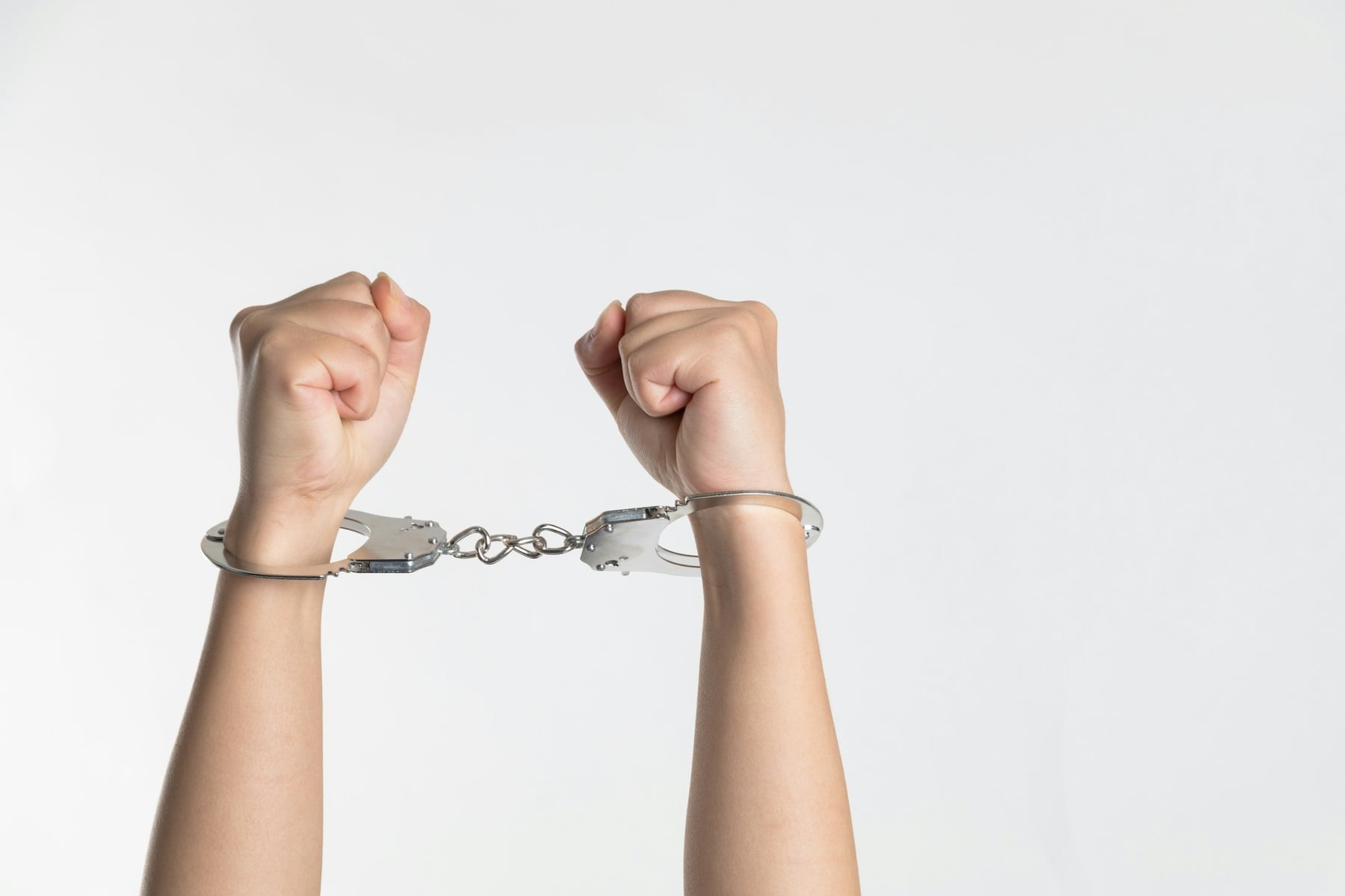Hands restrained in handcuffs against a white background